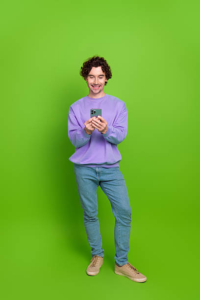 istock Young man in casual style using a smartphone while standing against a vibrant green backdrop 2235930496
