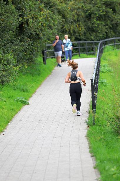 Gdansk, Poland - August 07, 2025: Woman running outdoors on a pathway next to foliage
