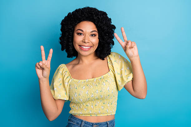istock Cheerful young woman making peace signs with both hands in front of a blue studio background 2235931291