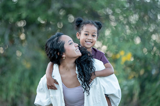 istock Smiling Mother and Daughter Piggyback Outdoors in a Sunny Forest Setting 2235939147