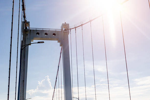 Sunlit suspension bridge tower against a clear blue sky.