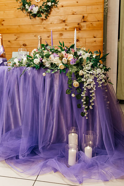 Table with purple tablecloth and flowers on it. There are candles on the table. The table is set for a wedding. Festive wedding table decoration