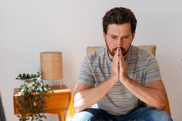 istock Pensive man reflecting with hands clasped at home 2235947173