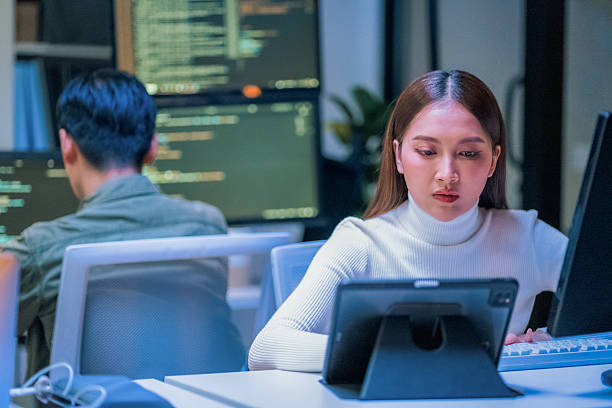istock young Asian software development manager leads a late-night office discussion with his executive team, mentoring developers and analyzing source code to guide programming and project development 2235948084