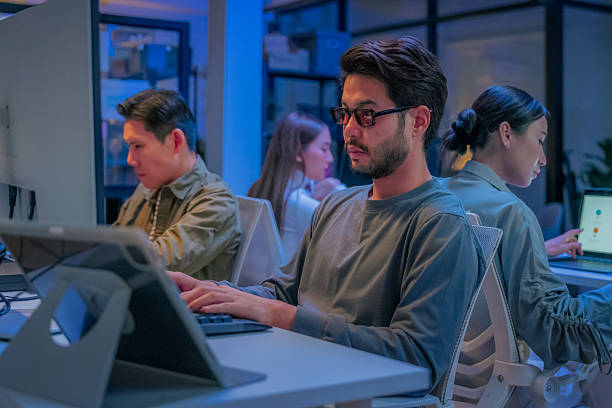 istock young Asian software development manager leads a late-night office discussion with his executive team, mentoring developers and analyzing source code to guide programming and project development 2235950485
