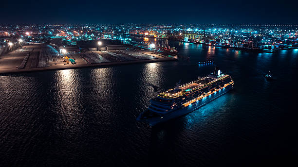cruise ship departs from the port at night, shutter is slow because it needs to be a movement of the boat, commercial port background, blue tone cinematic style, aerial view.
