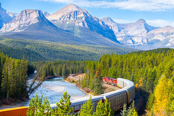 istock Freight train winding through Rocky Mountain landscape, passing clear river, flanked by pine and golden trees under azure sky during autumn season 2235952290