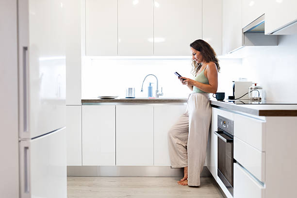 istock Young Caucasian woman at home kitchen leaning on counter while using smartphone 2235955006