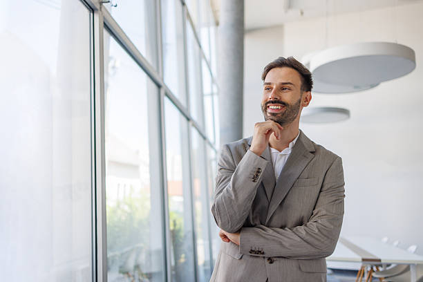 istock Pensive businessman looking out large office window and smiling 2235957295