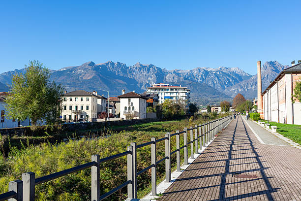 Pathway surrounded by greenery and buildings, leading towards stunning mountains, under a bright blue sky, illustrating the blend of nature and urban scenery of Feltre in the province of Belluno, Veneto, Italy,