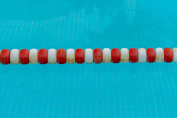 A close-up shows a row of red and white lane divider floats on a blue tiled swimming pool surface.
