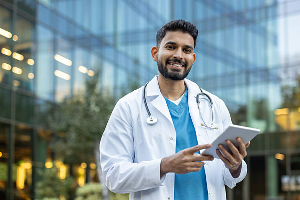 istock A smiling Indian doctor using a tablet outside a modern building in daylight. 2235972389