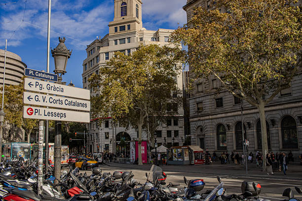Barcelona, Spain - Nov 23 2024: A view of Plaza de Catalunya Street in Barcleona during a sunny day. Some motorcycles are parked on the left side, the streer is partially visible.