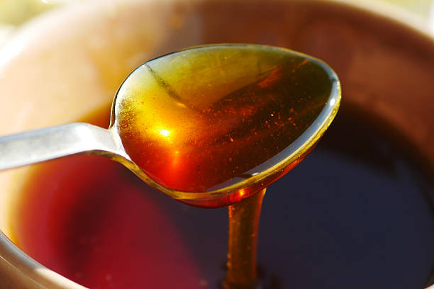 Sweet golden honey glistens as it drips from a spoon, capturing sunlight.