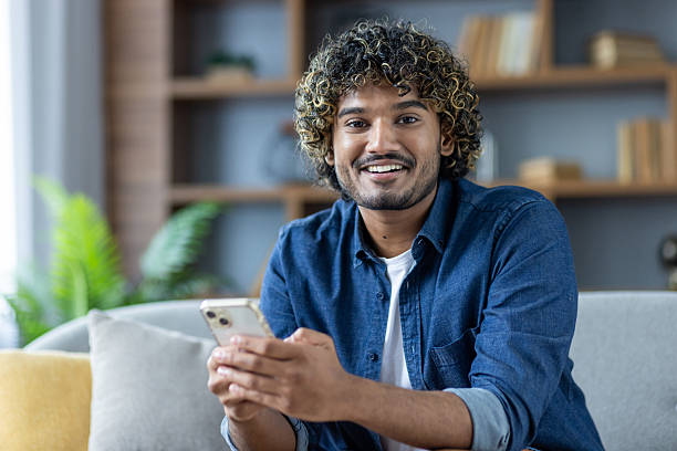 istock Smiling man holding smartphone at home with cozy interior 2235983639