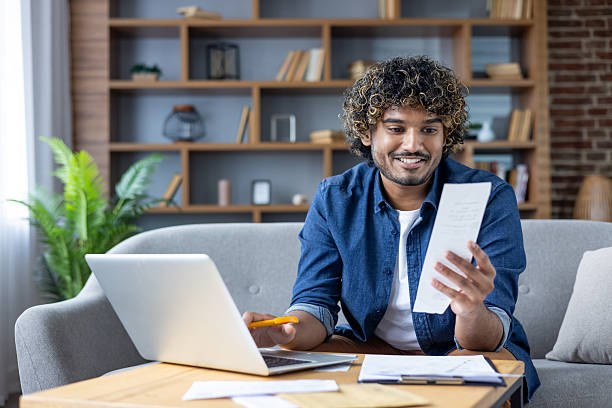 istock Smiling Man Working on Laptop and Reviewing Document at Home 2235983642