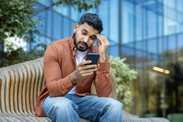 istock A thoughtful man checks his mobile phone while sitting outdoors with a serious expression. 2235986798