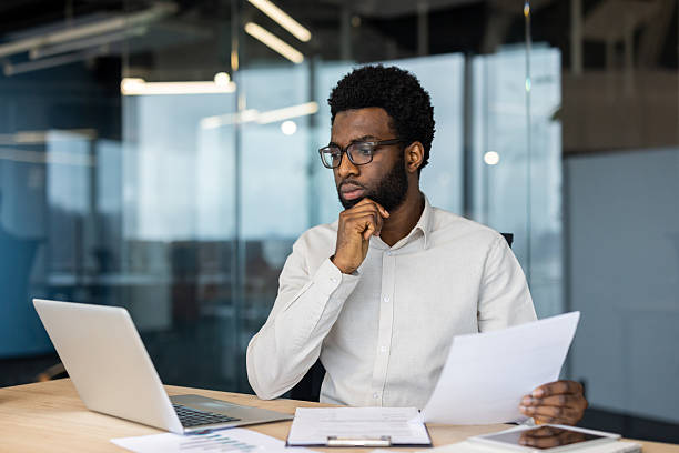 istock Pensive businessman reading documents and using laptop in office 2235987482