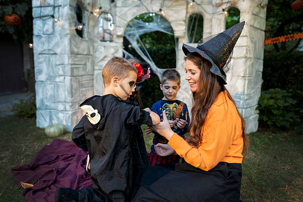 istock Halloween witch helping children with face and body art. 2235987509