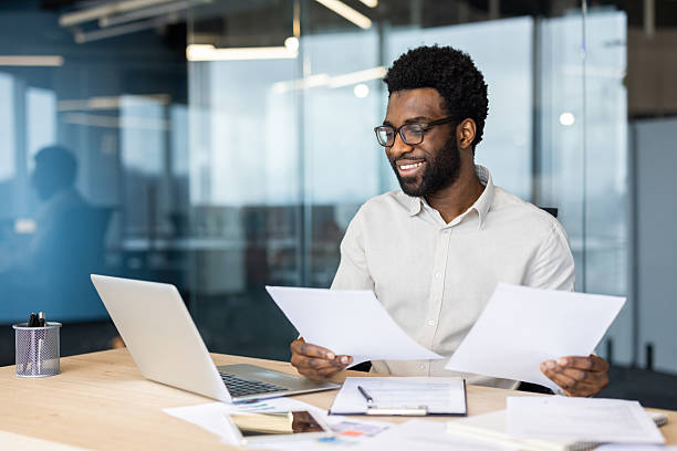istock A smiling businessman reviews paperwork while working at his desk with a laptop 2235987513