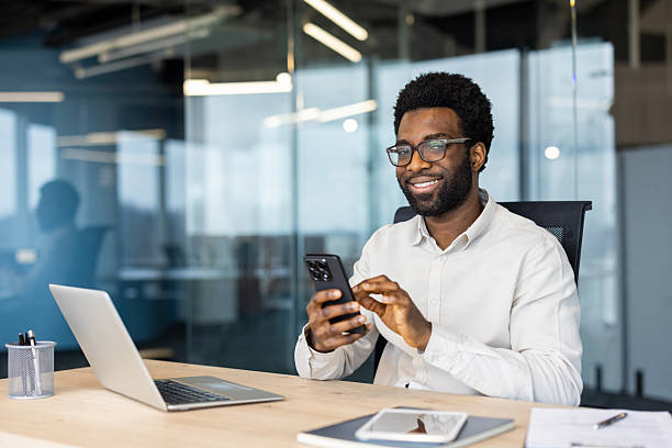 istock Smiling businessman using smartphone and laptop in modern office setting 2235987558