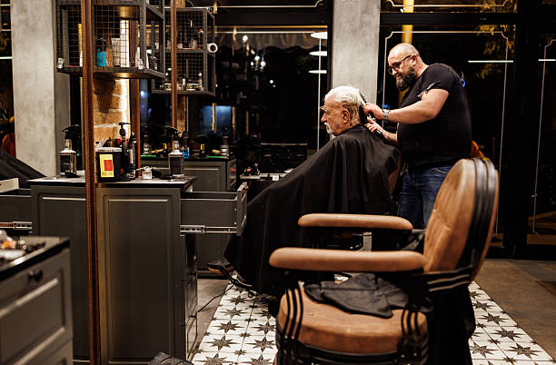 Professional barber dries hair of an elderly male client in a modern barbershop
