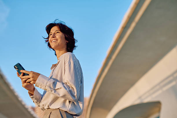 istock Businesswoman using smartphone smiling under bridge during sunset 2235994287