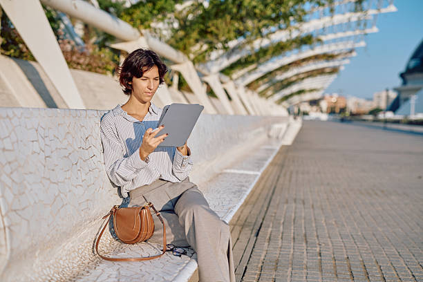 istock Businesswoman using tablet sitting on bench in a modern city 2235994611