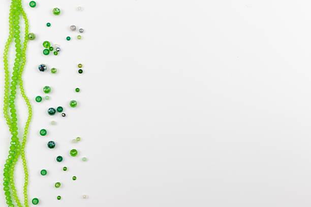 Top view on a white background shows green beads in various shades arranged as a decorative frame along the left side. Perfect for craft, DIY, jewelry making, decoration, advertising, marketing, banners, and creative projects. High quality photo