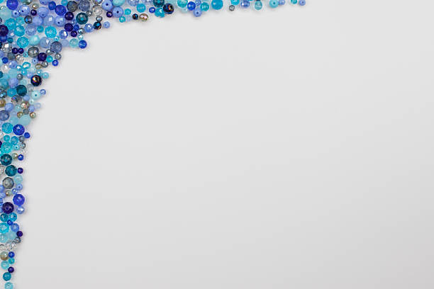 On a white background blue and light blue glass crystal beads of various sizes, both matte and transparent, form a decorative frame along the left and top sides, including the top left corner. Center and right side provide ample copy space. Perfect for jewelry, craft, DIY, decoration, advertising, marketing, and banners. High quality photo