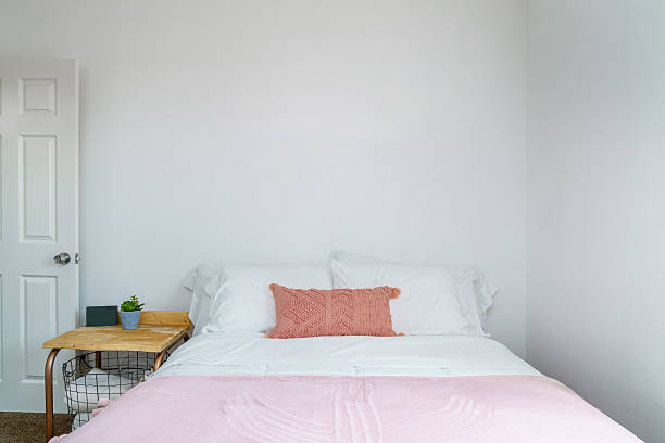 White bedroom with pink chenille pillow, throw blanket, and side table with basket. Front view.