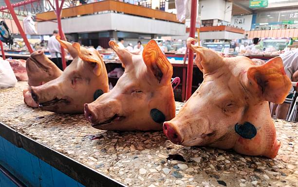 Three pig heads line a counter, displaying merchandise at a traditional meat market. The photo captures the realistic, if somewhat rough, atmosphere of a local market selling fresh meat.