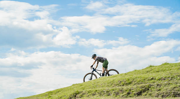 a man pedals on sandstone rock formations underneath a cloud filled blue sky.  horizontal composition taken at red rock park in gallup, new mexico.