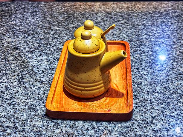 Two small mustard yellow ceramic teapots, likely for condiments or soy sauce, placed on a rectangular wooden tray on a gray granite tabletop
