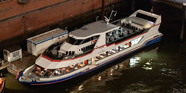 Hamburg, Germany – September 16, 2023: Night view of the passenger ferry Solar docked at the HafenCity pier. The ferry carries the signage Kapitän Prüsse. Illuminated windows reveal seating areas inside, while the red-brick warehouses of Hamburg’s harbor frame the background.