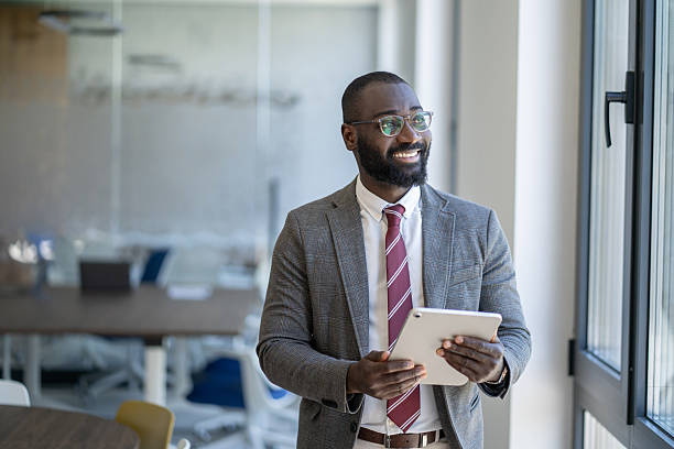 istock Smiling businessman holding digital tablet looking out office window 2236005545