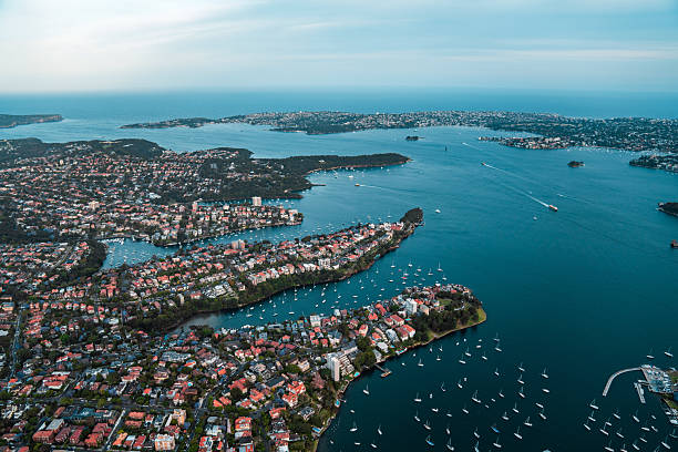 Aerial perspective of Sydney's prestigious waterfront neighborhoods featuring luxury residences, abundant moorings, and winding coastline along tranquil harbor waters.