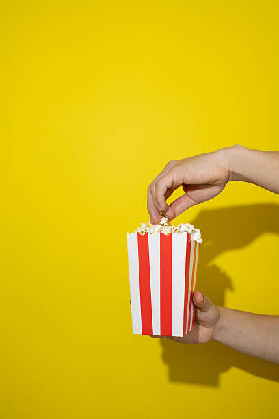 istock Hand taking popcorn from a cardboard box on a yellow background with copy space 2236007200