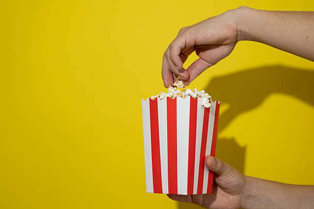 istock Hand taking popcorn from a cardboard box on a yellow background with copy space 2236007204