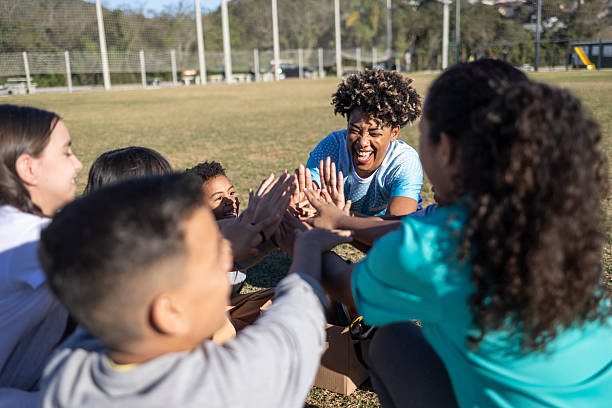 Medium shot of multiethnic kids point finger at camera and laugh outdoors. Diverse teenagers posing at camera and laughing outside in summer park