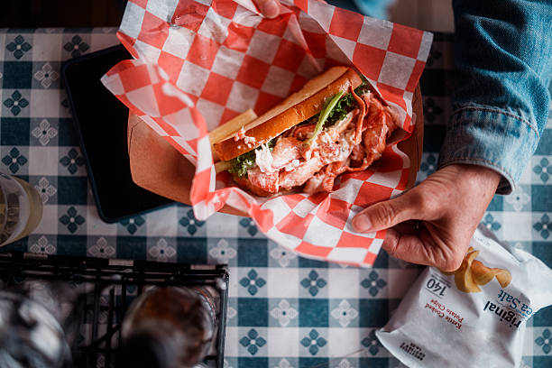 A fresh lobster roll with lettuce sits in a paper-lined basket on a checkered table at a casual seafood shack in Maine.