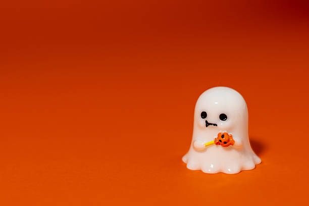 istock Cute white ghost figurine holding a pumpkin toy on an orange background with dramatic shadow and spotlight effect. Playful Halloween-themed image ideal for seasonal advertising, greeting cards, invitations, party decorations, children's designs 2236015786