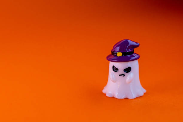 istock ghost wears a purple witch hat with evil look on an orange background under dramatic spotlight. Playful Halloween-themed decoration, perfect for seasonal advertising, greeting cards, party invitations, children's designs, and creative holiday projects. 2236015837