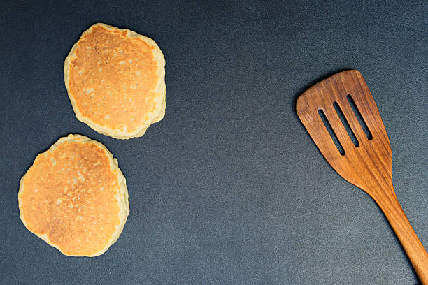 Caucasian redhead mother pours batter from ladle onto the skillet, frying crepes for daughter's tasty and quick breakfast. Selective focus on a ladle with batter and frying pan