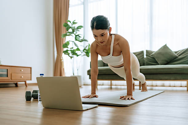 istock Young Asian woman in sportswear doing plank on training mat while watching online workout tutorials on laptop in the living room. Sport and recreation concept 2236017361