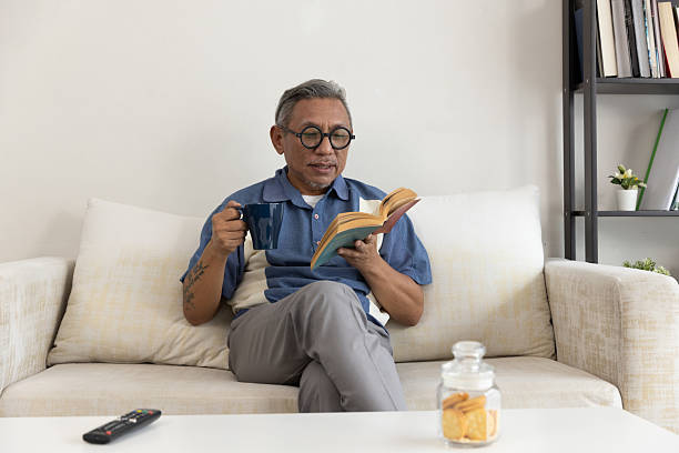 istock Older man enjoys reading a book while drinking coffee at home in a cozy living room setting 2236020032
