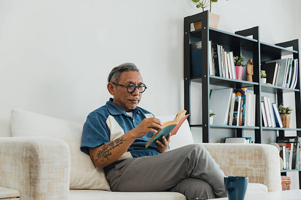 istock Older man reading a book comfortably while seated in a cozy living room setting 2236020726