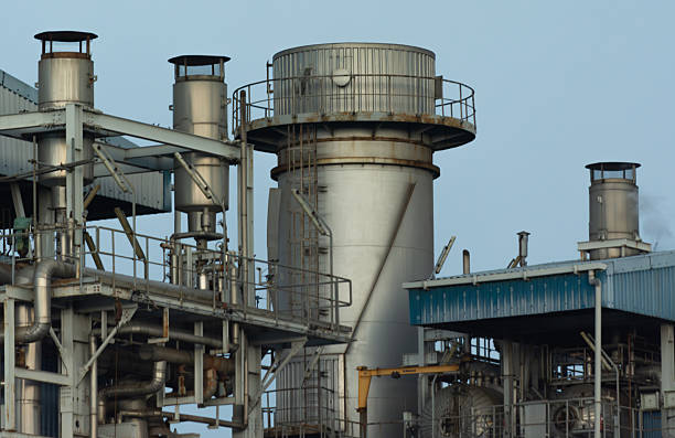 Stock image of a power plant facility operating under an overcast cloudy sky. The photo showcases the overall structure of the industrial complex, including pipelines, buildings, and supporting infrastructure. The cloudy atmosphere adds a dramatic tone to the image, emphasizing the scale and presence of the facility in its environment. Suitable for illustrating themes related to energy production, industry, infrastructure development, and environmental context in modern industrial landscapes.