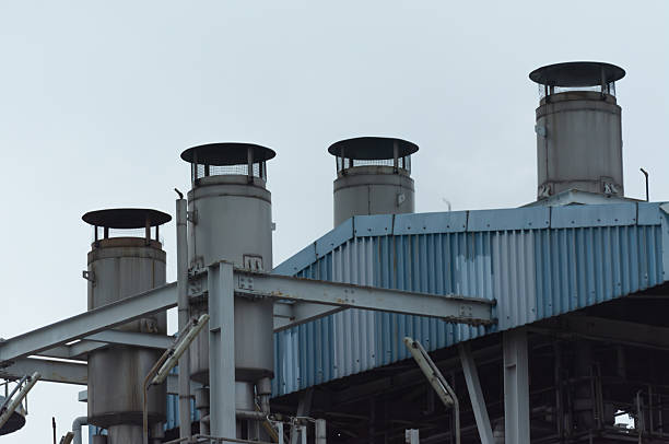 Stock image of a power plant facility operating under an overcast cloudy sky. The photo showcases the overall structure of the industrial complex, including pipelines, buildings, and supporting infrastructure. The cloudy atmosphere adds a dramatic tone to the image, emphasizing the scale and presence of the facility in its environment. Suitable for illustrating themes related to energy production, industry, infrastructure development, and environmental context in modern industrial landscapes.