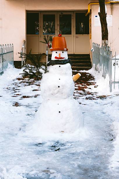 A cheerful snowman adorned with a scarf and carrot nose stands in a snow-covered square near Galata Tower in Beyoglu, Istanbul. The surrounding urban landscape, blanketed in fresh snow, captures the charm and seasonal beauty of this historic area during winter in Karakoy, Taksim, Turkey